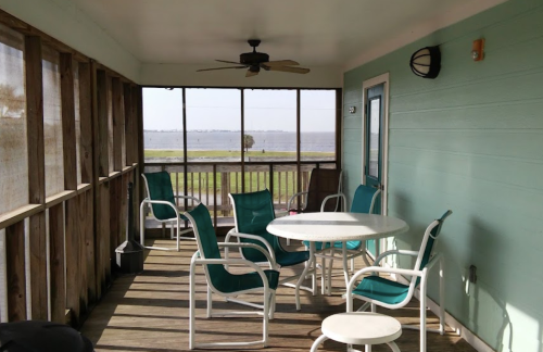 A screened porch with a round table and chairs, overlooking a scenic view of water and greenery.