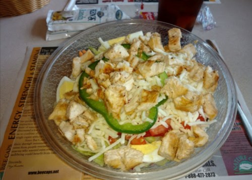 A glass bowl filled with a salad featuring chopped chicken, green peppers, tomatoes, and shredded cheese.