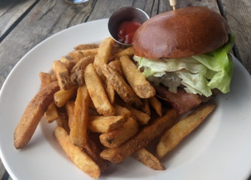 A plate with a burger topped with lettuce and a side of golden, crispy French fries and a small cup of ketchup.