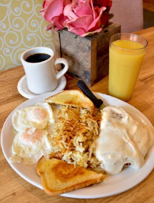 A plate of breakfast with eggs, hash browns, toast, sausage gravy, coffee, orange juice, and a flower centerpiece.