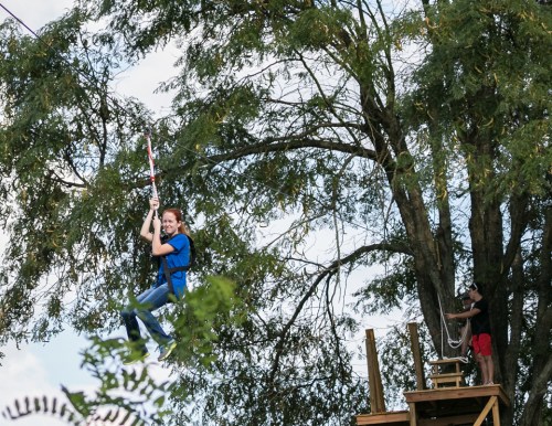 A person zip-lining through trees, while another individual stands on a platform nearby.