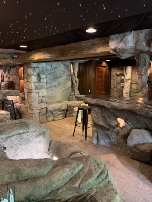 A rustic interior with stone walls and a starry ceiling, featuring natural rock formations and wooden accents.