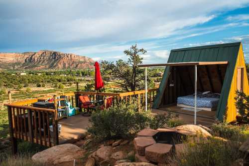 A colorful cabin on a deck with outdoor seating, surrounded by scenic mountains and greenery under a blue sky.