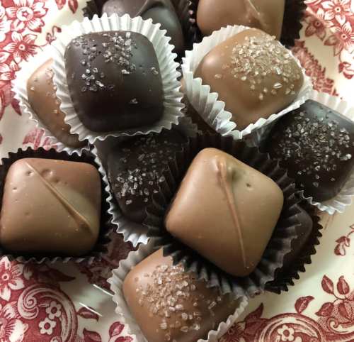A variety of chocolate candies in dark and milk chocolate, topped with coarse sugar, arranged in decorative cups.