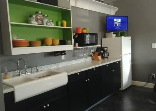 Modern kitchen with a farmhouse sink, black cabinets, green accents, and a TV mounted on the wall.