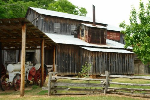 A rustic wooden barn with a metal roof, surrounded by trees and a vintage tractor in front.