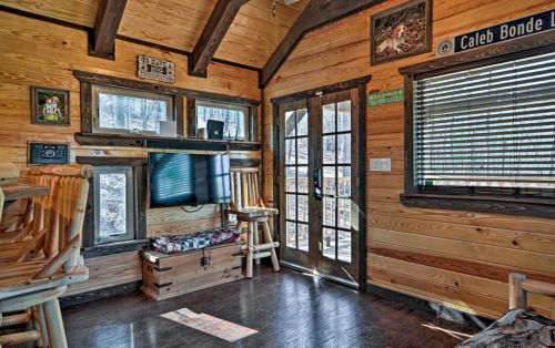 Cozy wooden interior of a cabin with a TV, chairs, and large windows letting in natural light.