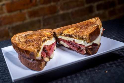 A toasted sandwich with layers of melted cheese and sliced meat, served on a white plate against a rustic background.