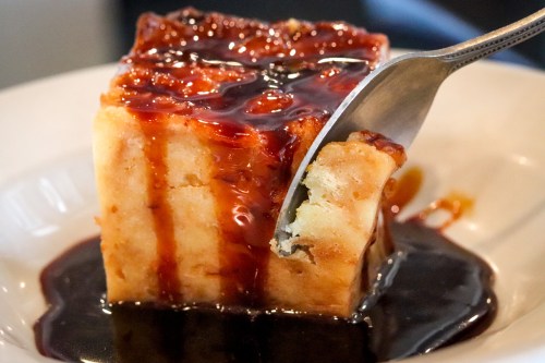 A piece of dessert with a glossy caramel sauce drizzled over it, resting on a white plate with a fork.