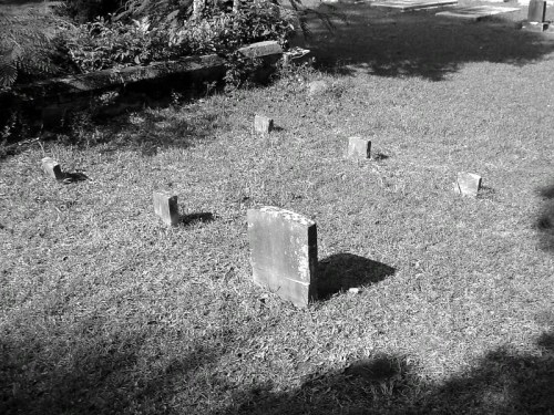 A black and white image of several weathered gravestones arranged in a grassy area.