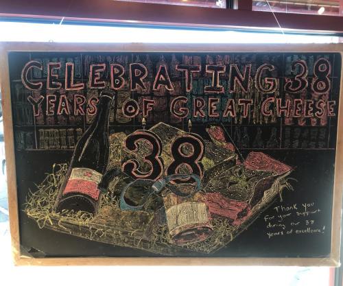 Chalkboard sign celebrating 38 years of great cheese, featuring wine bottles and a thank you message.