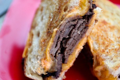 Close-up of a toasted sandwich filled with layers of beef and melted cheese on a red plate.