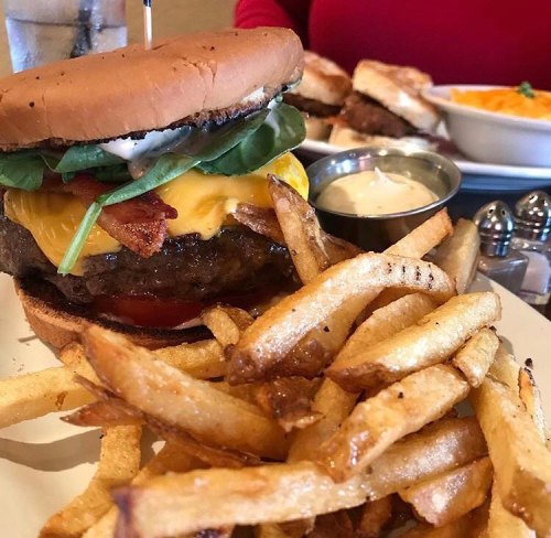 A juicy cheeseburger with bacon, lettuce, and tomato, served with crispy fries on a plate.