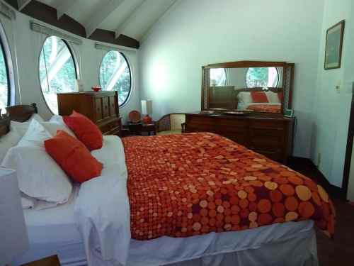 Cozy bedroom with a round window, featuring a bed with an orange dotted blanket and wooden furniture.