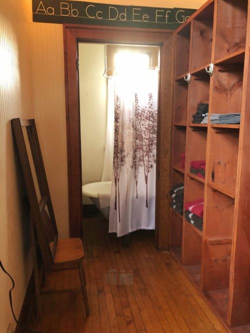 A small room with wooden shelves, a chair, and a curtain with tree designs leading to a bathroom area.