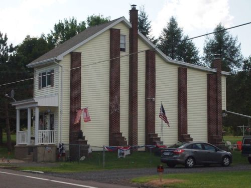 A two-story house with a mix of brick and yellow siding, featuring American flags and decorative bunting.