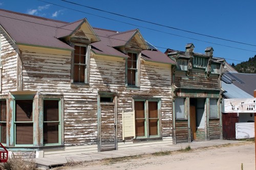 Abandoned wooden buildings with peeling paint and boarded windows under a clear blue sky.