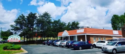 A restaurant building with a sign, surrounded by trees and parked cars under a partly cloudy sky.