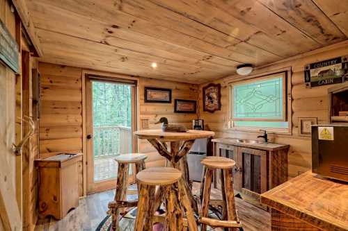 Cozy wooden cabin interior with a small dining area, bar stools, and a view of the outdoors through a glass door.