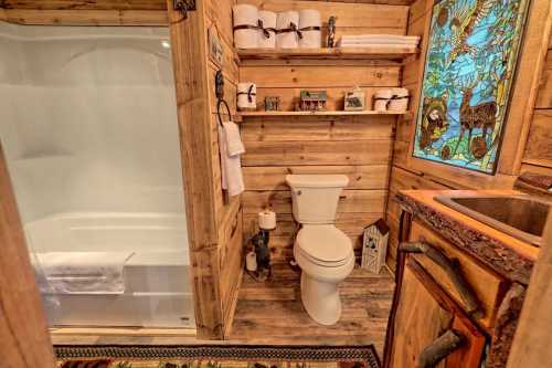 Cozy wooden bathroom featuring a shower, toilet, decorative shelves, and a stained glass window.