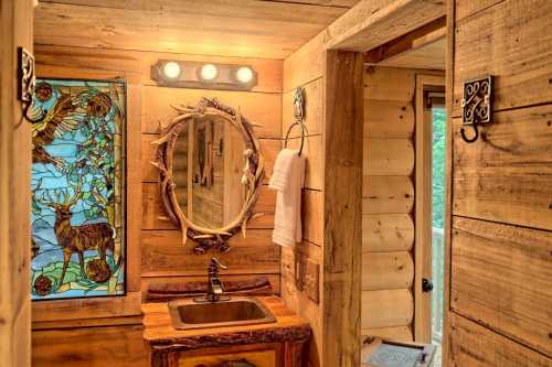 Cozy wooden bathroom featuring a stained glass window, antler mirror, and rustic sink with natural decor.