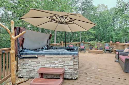 A wooden deck with a hot tub, umbrella, and seating area surrounded by trees.