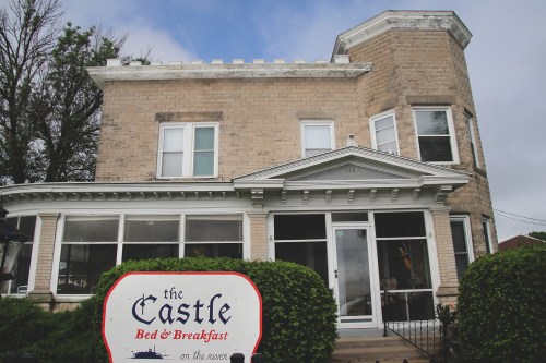 A charming stone bed and breakfast with a sign reading "The Castle" in front, surrounded by greenery.