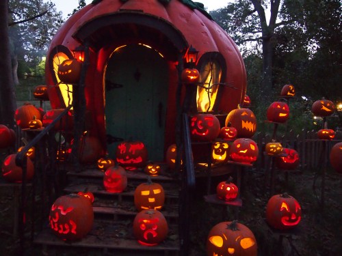 A whimsical pumpkin-shaped house surrounded by glowing jack-o'-lanterns on a dark evening.