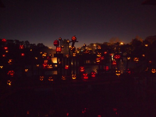 A dark scene featuring numerous glowing jack-o'-lanterns scattered around a body of water, creating a spooky atmosphere.