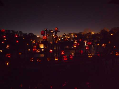 A dark scene featuring numerous glowing jack-o'-lanterns scattered around a body of water, creating a spooky atmosphere.