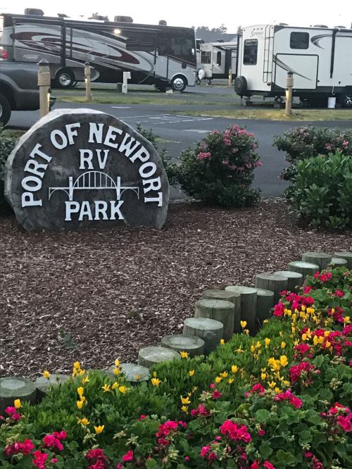 Sign for "Port of Newport RV Park" with colorful flowers and RVs in the background.