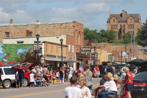 A busy street scene with people gathered, shops lining the road, and a historic building on a hill in the background.