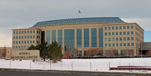 A modern municipal building with large windows, surrounded by snow, featuring a sign that reads "Aurora Municipal Center."
