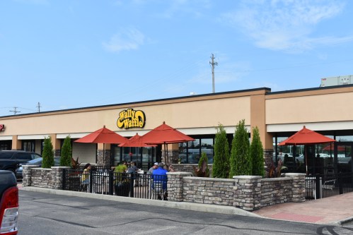 Exterior view of Wally Waffle restaurant with outdoor seating and umbrellas, surrounded by greenery and a stone wall.