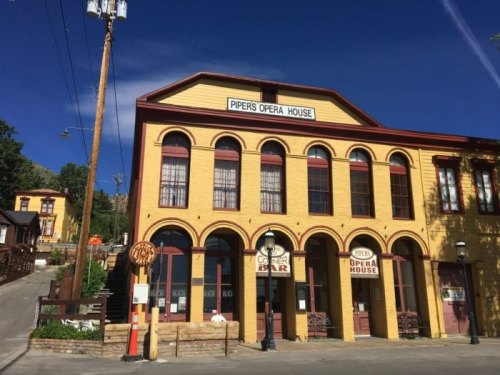 Historic yellow building with large windows, labeled "Piper's Opera House," set against a clear blue sky.
