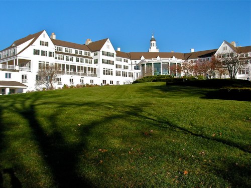 A large white hotel building with a green lawn in front, under a clear blue sky.