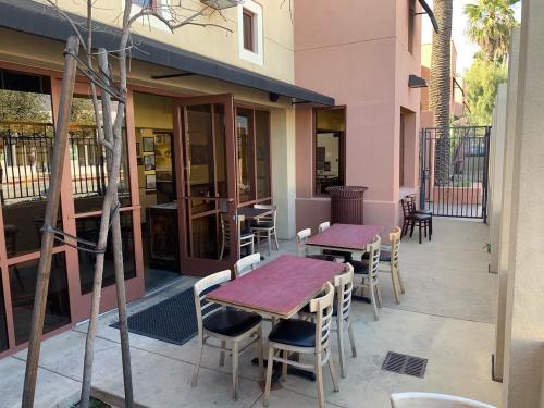 Outdoor seating area with tables and chairs next to a building, surrounded by a fence and trees.