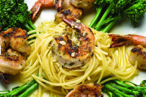 A plate of pasta topped with grilled shrimp and surrounded by vibrant green broccolini.