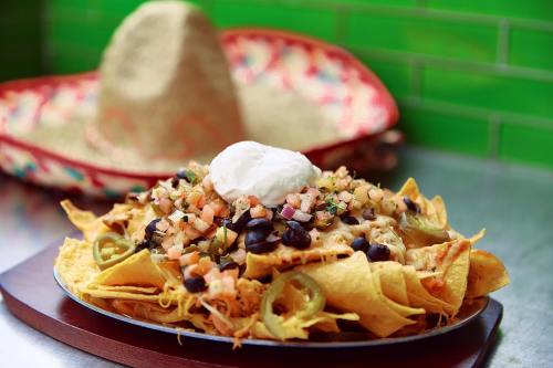 A plate of nachos topped with cheese, black beans, pico de gallo, jalapeños, and a dollop of sour cream.