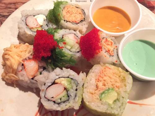 A plate of assorted sushi rolls with colorful toppings and two dipping sauces on the side.