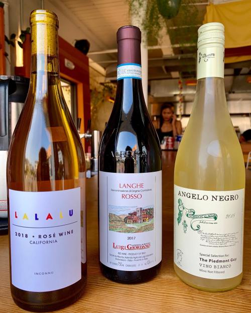 Three wine bottles on a table: a rosé, a red wine, and a white wine, with a blurred background of a restaurant.