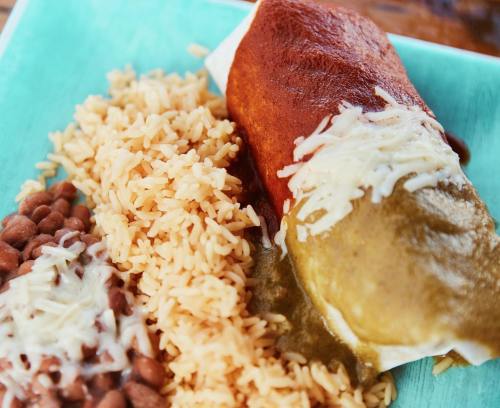 A plate featuring a burrito topped with sauce and cheese, served with rice and refried beans on a turquoise background.