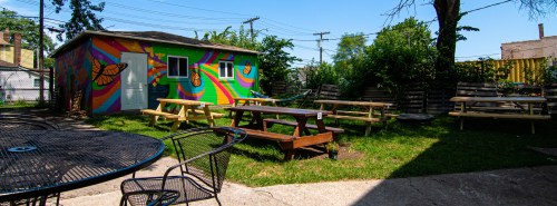 Colorful outdoor space with picnic tables, a vibrant mural on a shed, and greenery under a clear blue sky.