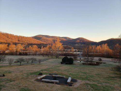 Scenic view of mountains with autumn foliage, a grassy area, and a fire pit in the foreground under a clear sky.
