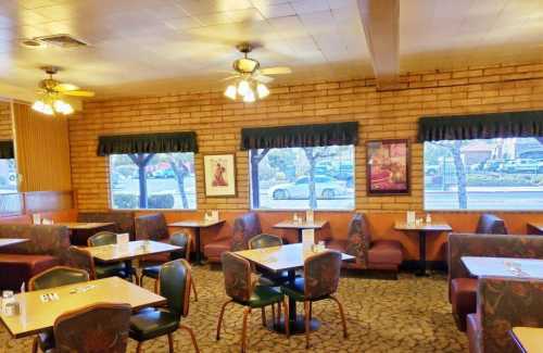 Cozy restaurant interior with wooden walls, tables, and chairs, featuring large windows and ceiling fans.