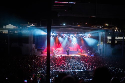 A vibrant concert scene with a large crowd under colorful stage lights at night.
