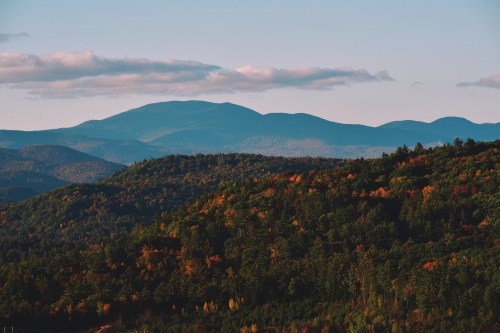 A scenic view of rolling mountains covered in lush greenery and autumn foliage under a clear blue sky.