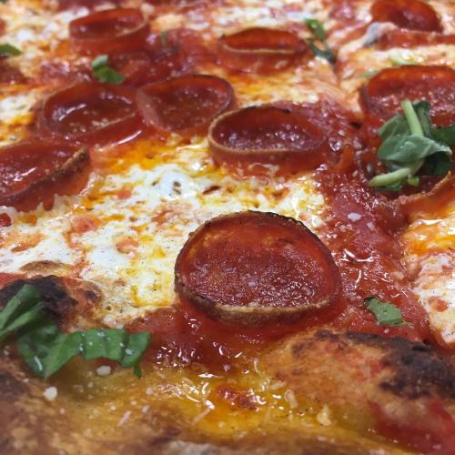 Close-up of a pepperoni pizza with melted cheese, tomato sauce, and fresh basil leaves.