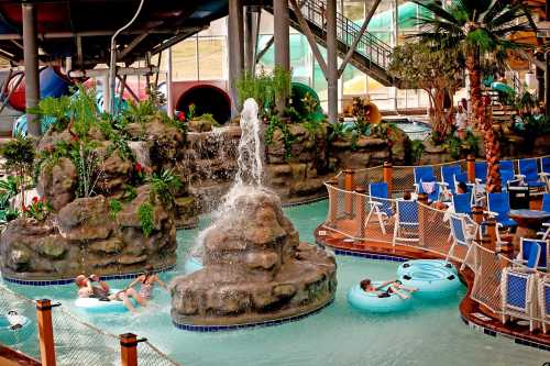 Indoor water park scene with a waterfall, lazy river, and guests relaxing on floaties surrounded by tropical plants.