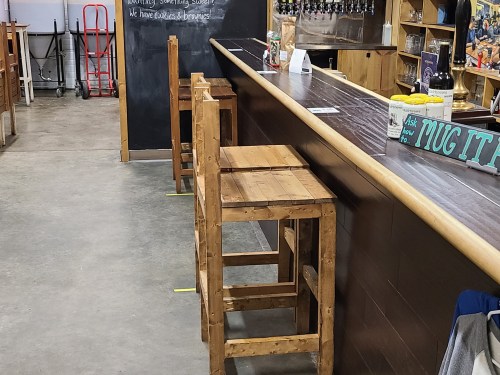 A wooden bar with high stools, a chalkboard menu, and a spacious interior in a casual setting.